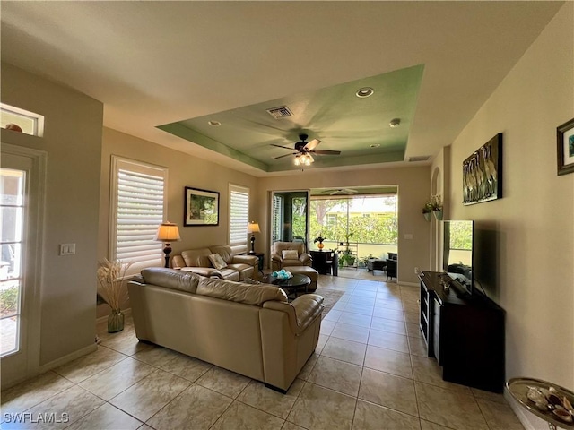 living room featuring light tile patterned floors, ceiling fan, and a raised ceiling