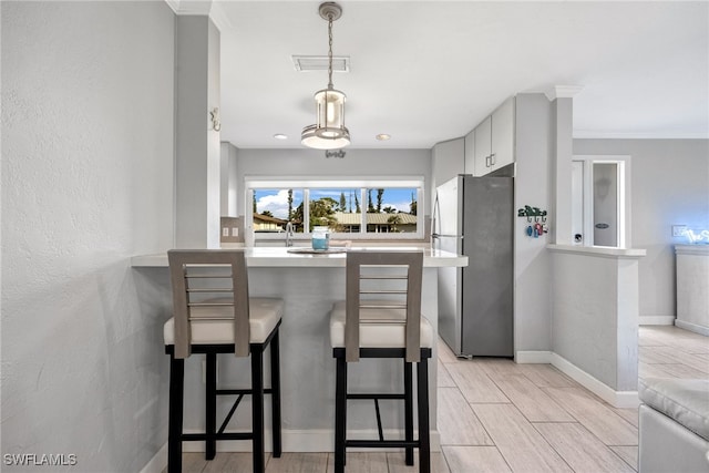 kitchen featuring crown molding, stainless steel refrigerator, a breakfast bar, hanging light fixtures, and kitchen peninsula