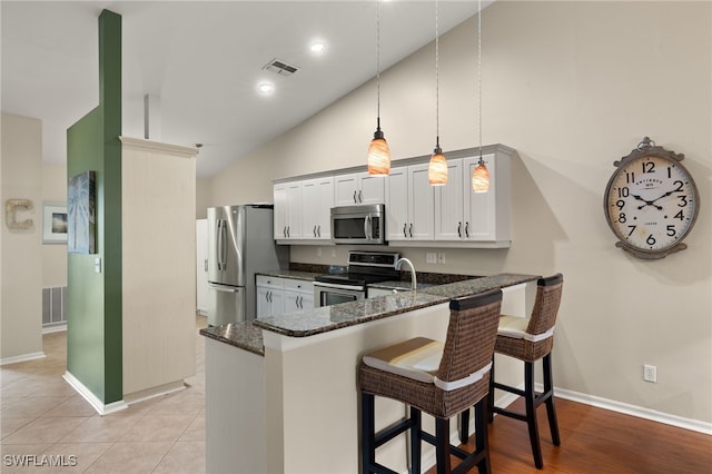 kitchen with dark stone countertops, a peninsula, hanging light fixtures, stainless steel appliances, and a kitchen bar