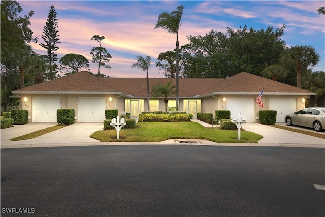 single story home featuring a garage, driveway, a lawn, and stucco siding