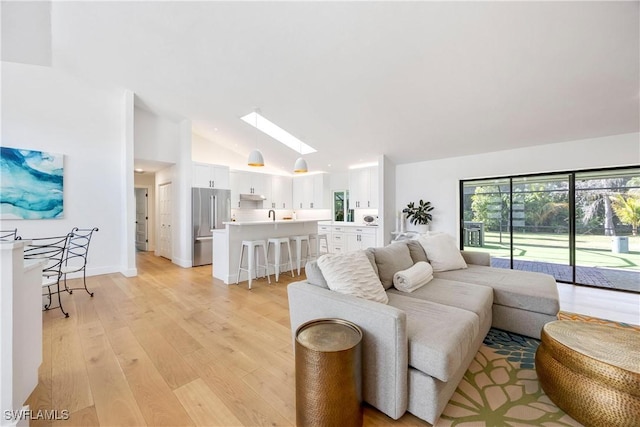 living room featuring high vaulted ceiling, light wood-type flooring, and a skylight