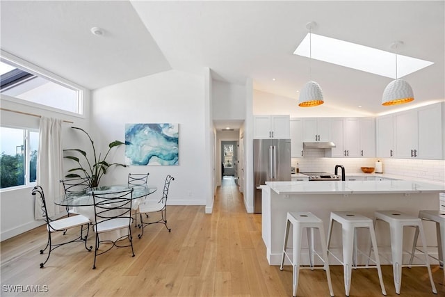 kitchen with a breakfast bar, white cabinetry, tasteful backsplash, stainless steel fridge, and pendant lighting