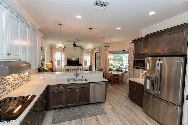 kitchen with appliances with stainless steel finishes, decorative light fixtures, sink, kitchen peninsula, and light hardwood / wood-style flooring