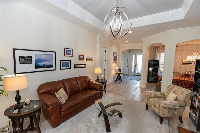 living room featuring a raised ceiling, crown molding, a chandelier, and light hardwood / wood-style floors