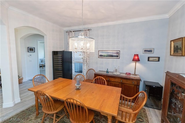 dining area featuring crown molding, a chandelier, beverage cooler, and light wood-type flooring