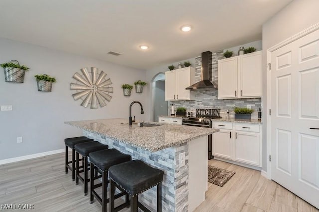 kitchen featuring sink, an island with sink, white cabinets, and wall chimney exhaust hood