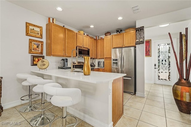 kitchen featuring light tile patterned floors, a breakfast bar area, stainless steel appliances, and kitchen peninsula