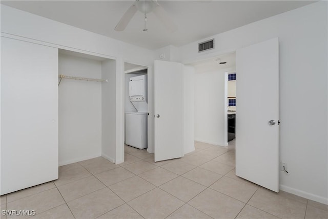 unfurnished bedroom with light tile patterned flooring, ceiling fan, stacked washing maching and dryer, and a closet