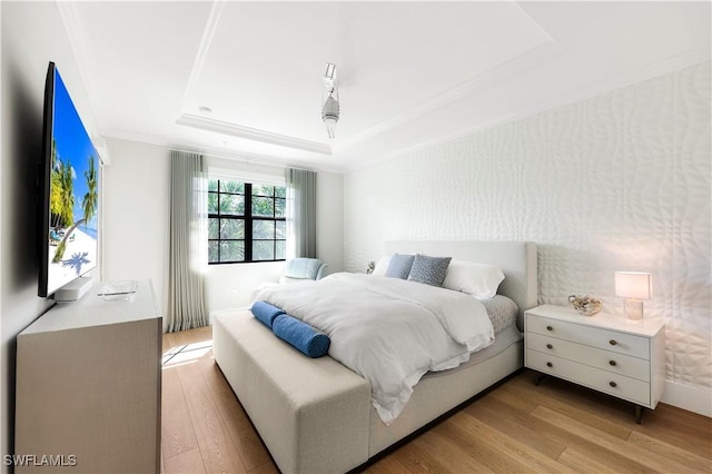 bedroom with crown molding, a raised ceiling, and light wood-type flooring