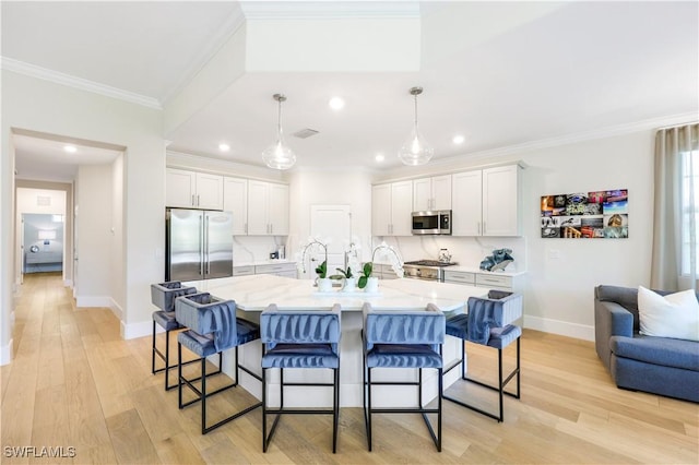 kitchen with white cabinetry, premium appliances, hanging light fixtures, and an island with sink