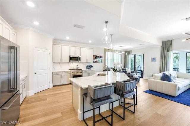 kitchen with white cabinetry, an island with sink, sink, premium appliances, and light stone counters