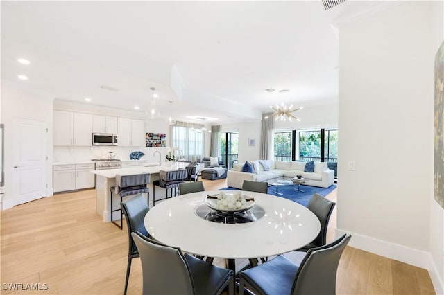 dining space featuring an inviting chandelier, sink, and light hardwood / wood-style flooring