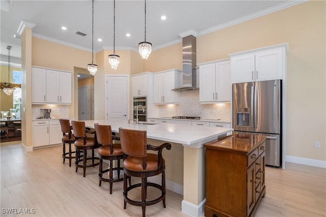 kitchen with appliances with stainless steel finishes, pendant lighting, white cabinetry, a center island with sink, and wall chimney exhaust hood