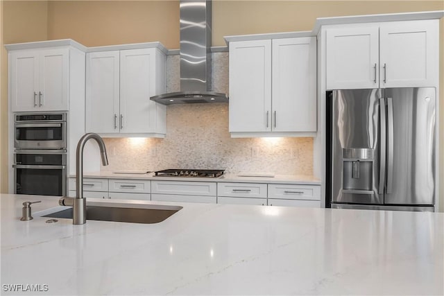 kitchen with wall chimney range hood, stainless steel appliances, sink, and light stone countertops