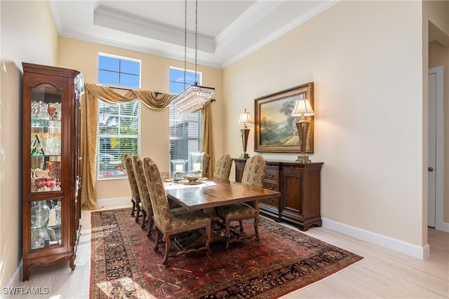 dining area featuring a raised ceiling, crown molding, and light wood-type flooring