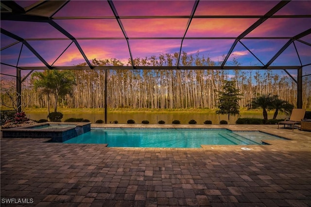 pool at dusk with a patio area, an in ground hot tub, and glass enclosure