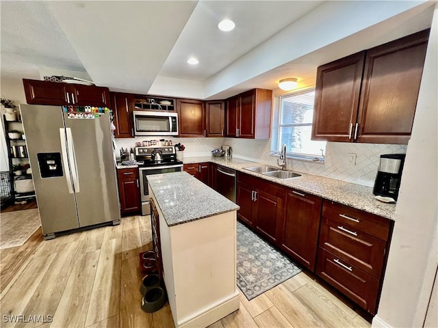 kitchen featuring sink, appliances with stainless steel finishes, light stone counters, light hardwood / wood-style floors, and a kitchen island