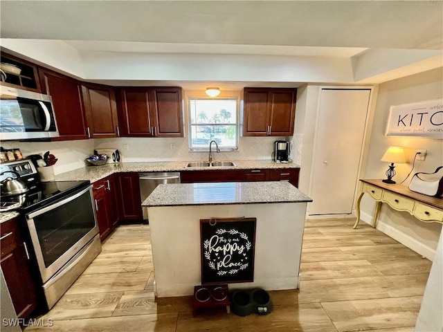 kitchen with a kitchen island, appliances with stainless steel finishes, sink, light stone counters, and light hardwood / wood-style flooring