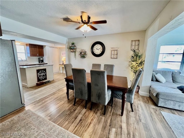 dining area with ceiling fan, plenty of natural light, a textured ceiling, and light hardwood / wood-style flooring