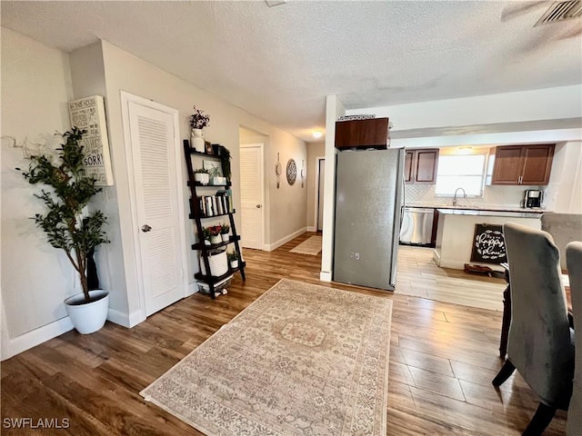 interior space featuring appliances with stainless steel finishes, a textured ceiling, light hardwood / wood-style floors, and decorative backsplash