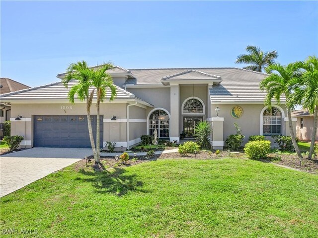 view of front of property with an attached garage, stucco siding, a front lawn, a tiled roof, and decorative driveway