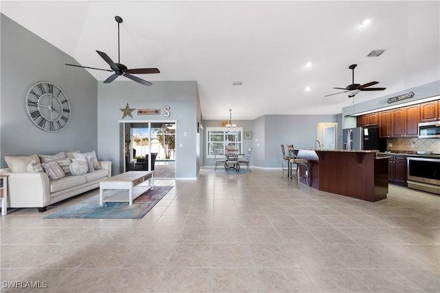 living room with lofted ceiling, light tile patterned floors, and ceiling fan with notable chandelier