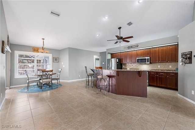 kitchen featuring appliances with stainless steel finishes, a kitchen island with sink, hanging light fixtures, a kitchen breakfast bar, and tasteful backsplash