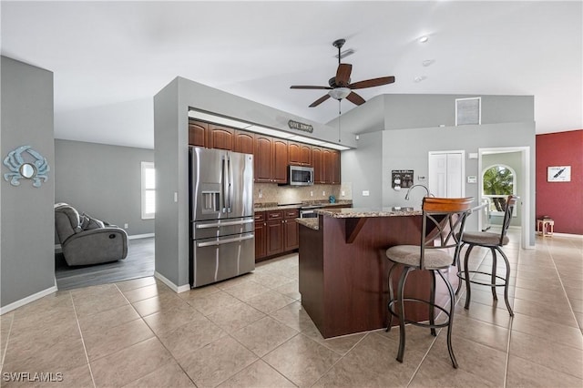 kitchen with a kitchen bar, vaulted ceiling, a center island with sink, stainless steel appliances, and light stone countertops