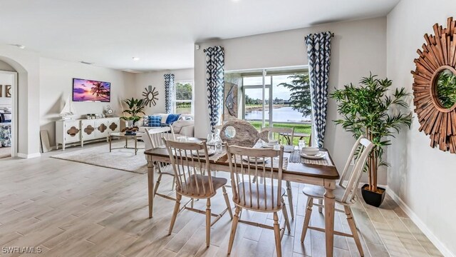 dining space with light wood-style flooring, arched walkways, and baseboards