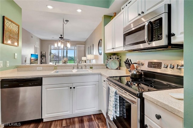 kitchen featuring decorative light fixtures, appliances with stainless steel finishes, dark wood-type flooring, white cabinets, and a sink