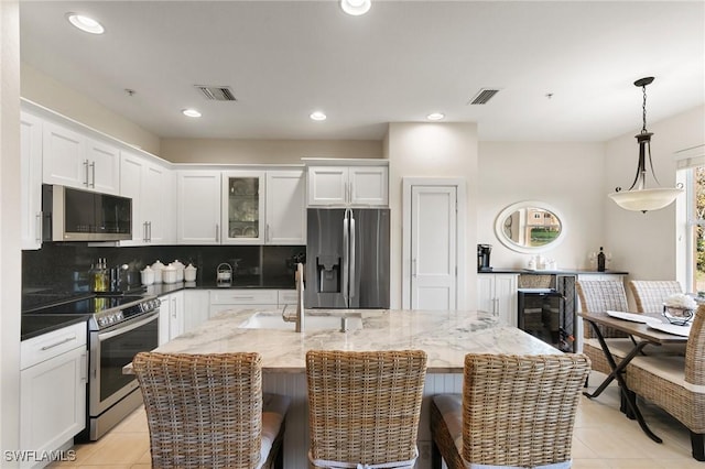 kitchen with white cabinetry, dark stone countertops, appliances with stainless steel finishes, an island with sink, and pendant lighting