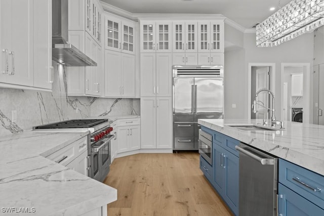 kitchen featuring built in appliances, white cabinetry, wall chimney exhaust hood, and blue cabinets