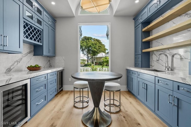 interior space featuring wine cooler, blue cabinets, sink, and light stone counters