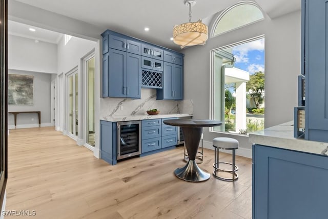 bar featuring beverage cooler, decorative backsplash, light stone countertops, blue cabinetry, and light hardwood / wood-style flooring