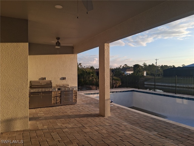 patio terrace at dusk with ceiling fan, grilling area, and an outdoor kitchen