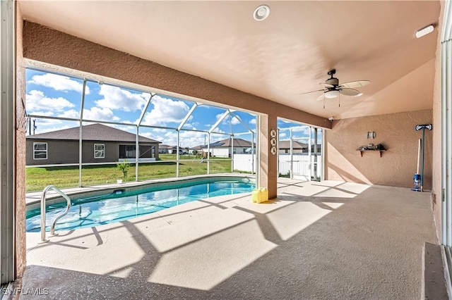 view of swimming pool with a yard, a patio area, ceiling fan, and glass enclosure