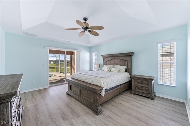 bedroom featuring multiple windows, light hardwood / wood-style floors, and a raised ceiling