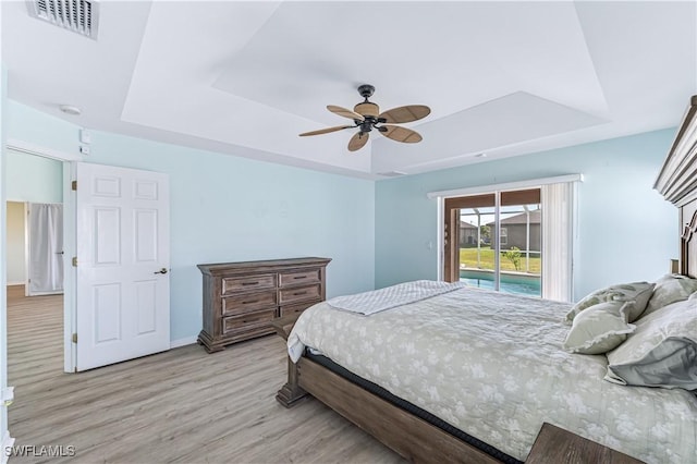 bedroom featuring ceiling fan, access to outside, light hardwood / wood-style floors, and a tray ceiling