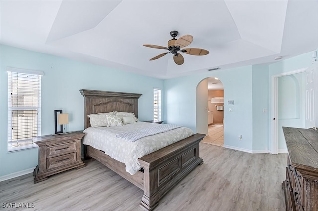 bedroom with multiple windows, a raised ceiling, and light wood-type flooring