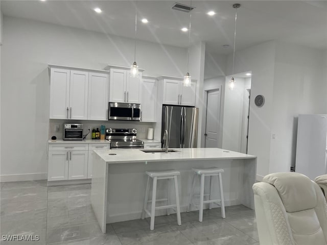 kitchen with appliances with stainless steel finishes, decorative light fixtures, white cabinetry, sink, and a center island with sink