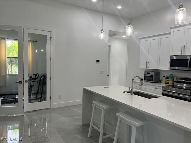 kitchen featuring sink, white cabinetry, hanging light fixtures, stainless steel appliances, and light stone countertops