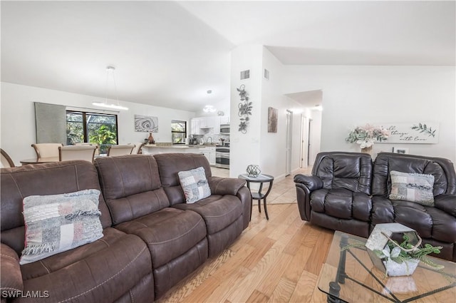 living room featuring lofted ceiling, light wood-type flooring, and visible vents