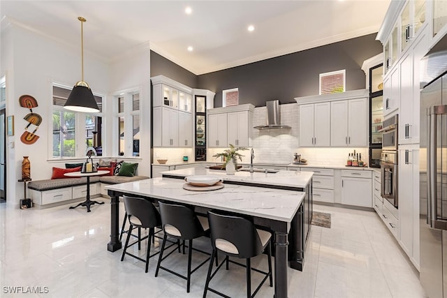 kitchen with a center island with sink, a breakfast bar area, backsplash, light stone countertops, and wall chimney exhaust hood