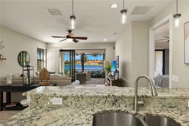 kitchen with hardwood / wood-style floors, sink, hanging light fixtures, ceiling fan, and light stone countertops