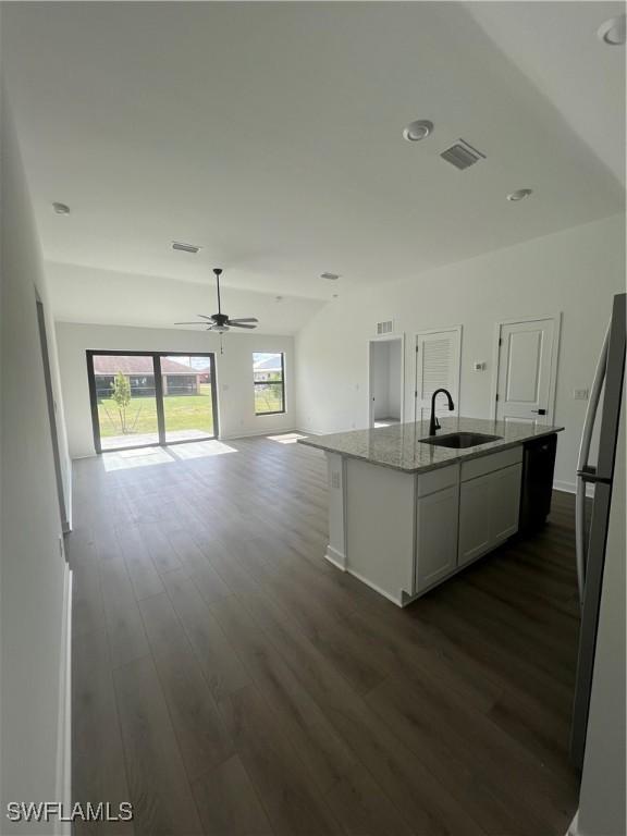 kitchen featuring sink, dark wood-type flooring, stainless steel refrigerator, light stone countertops, and an island with sink