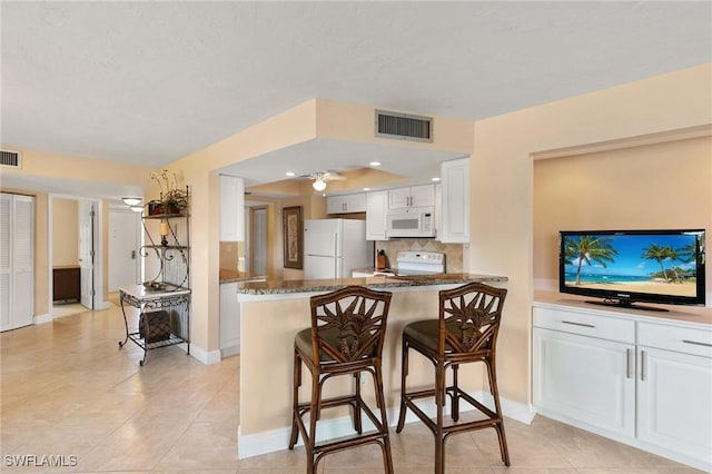 kitchen with a kitchen bar, tasteful backsplash, white appliances, dark stone counters, and white cabinets