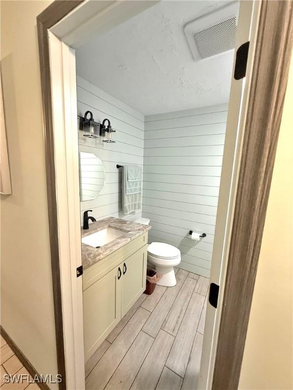 bathroom featuring vanity, toilet, and wood walls