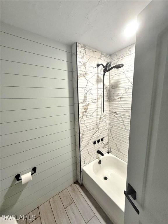 bathroom featuring tiled shower / bath and wood walls