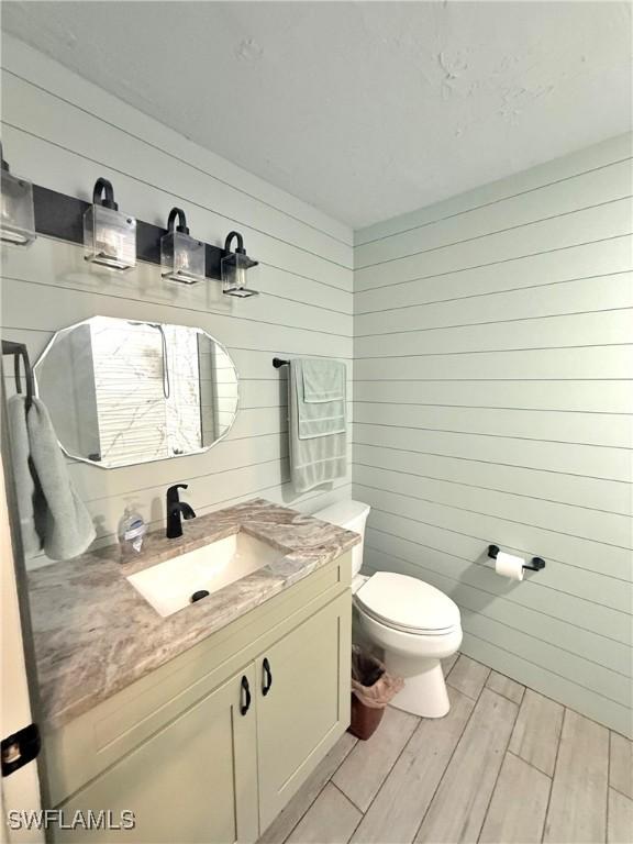 bathroom featuring vanity, toilet, and wood walls