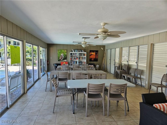 dining area featuring light tile patterned floors, wooden walls, and ceiling fan